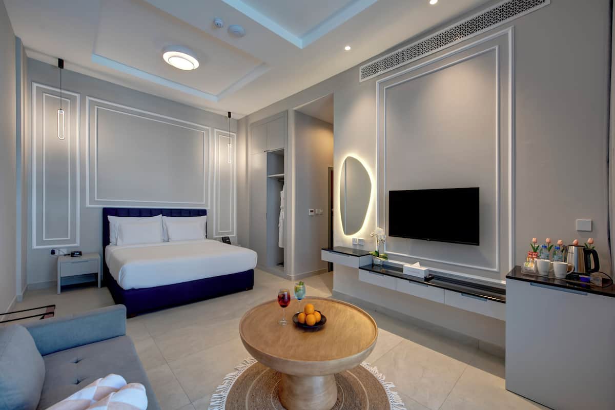 Una habitación de hotel moderna con una cama grande, televisión, mesa de comedor y zona de estar.