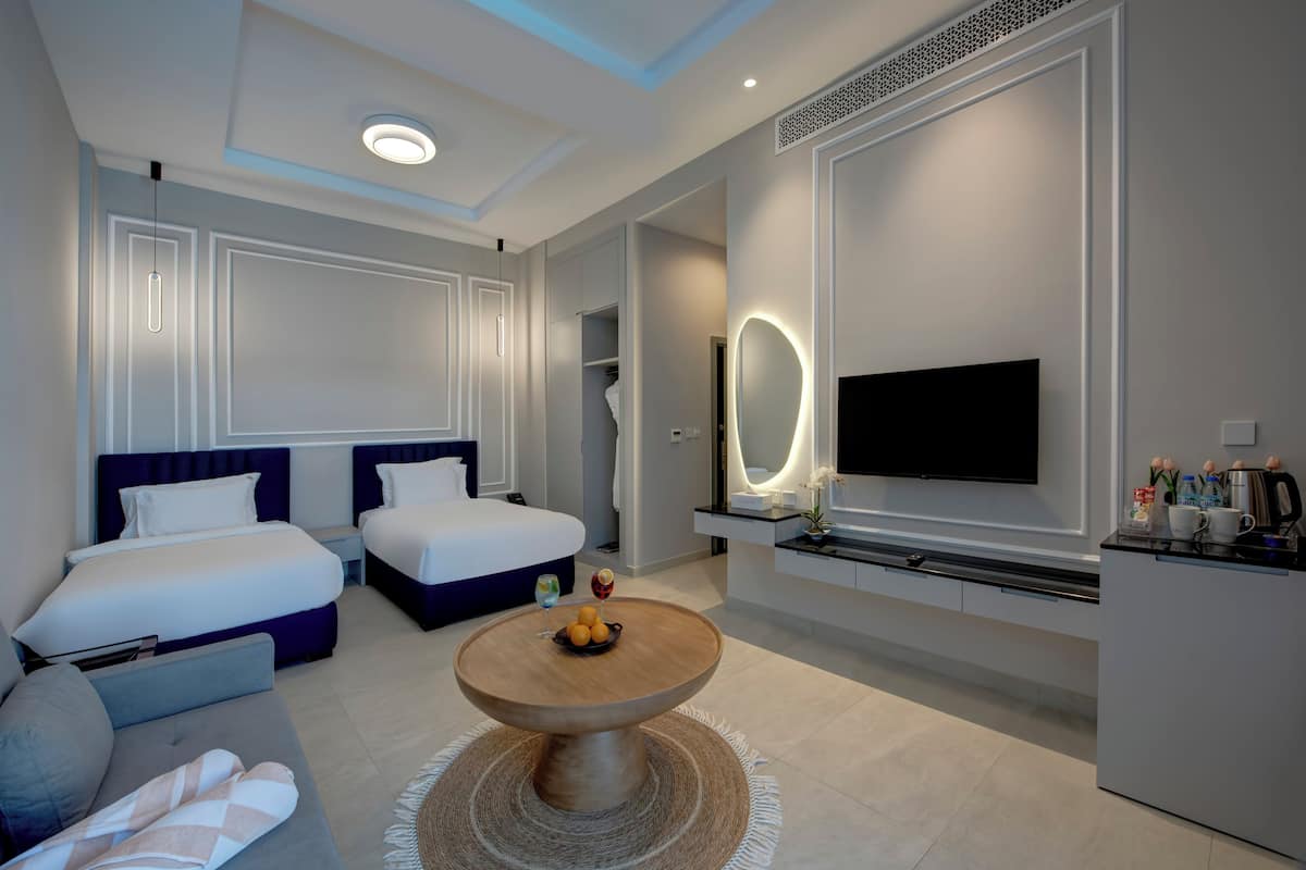 Una habitación de hotel moderna con dos camas, televisión, zona de comedor y baño.