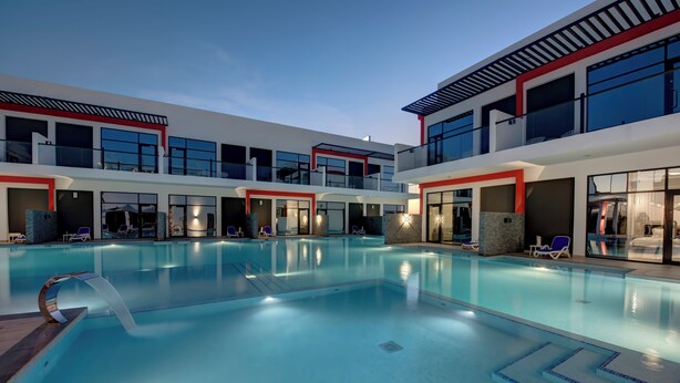 A modern hotel with a large indoor swimming pool, multiple balconies, and a contemporary design. - KAY Homes (Ras Al Khaimah)
