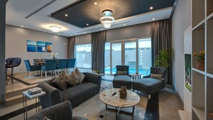 A modern living room with grey sofas, a coffee table, and a dining area with blue chairs. - KAY Homes (Ras Al Khaimah)