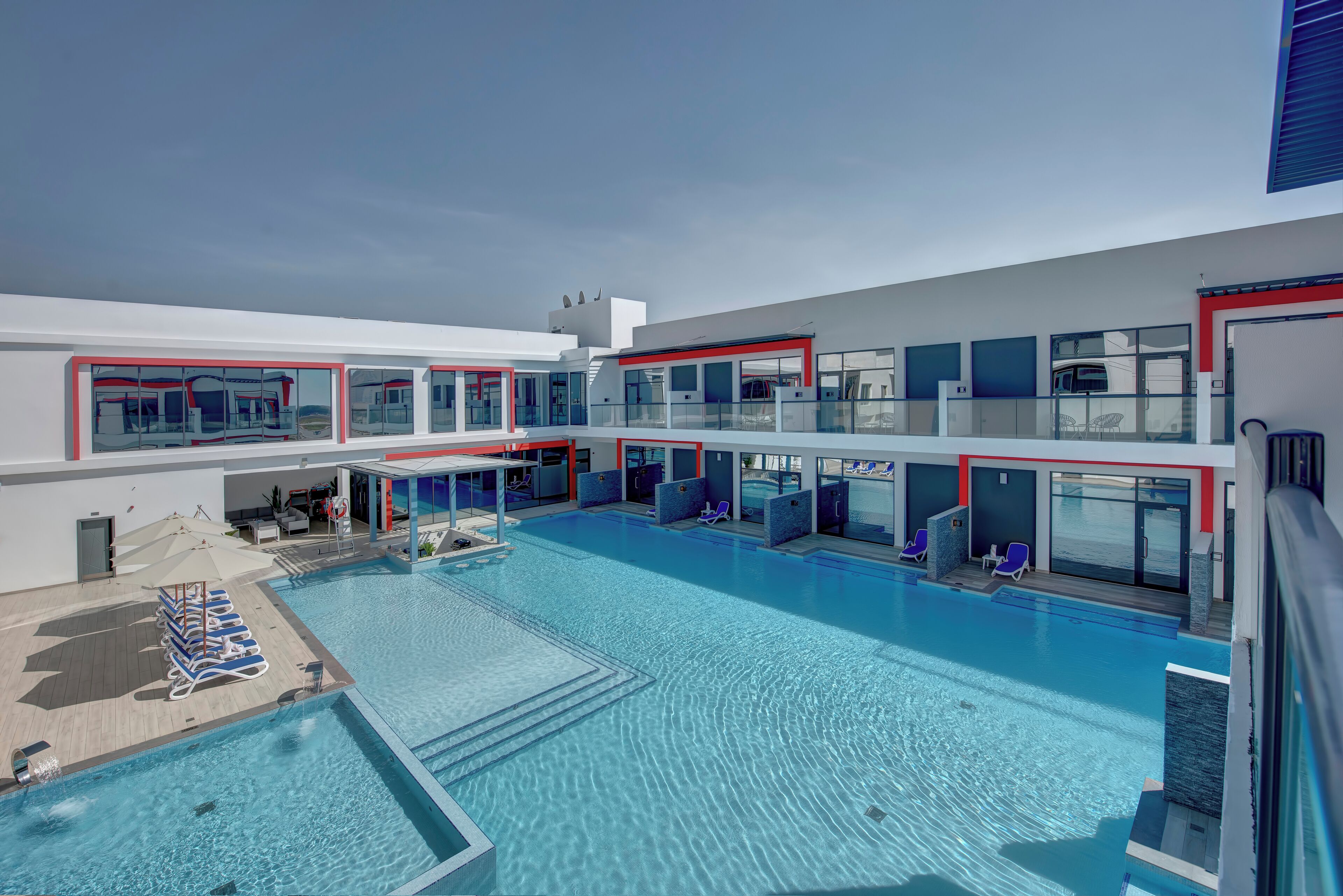 A modern hotel with a large indoor pool, multiple balconies, and sun loungers.