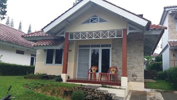 A two-story house with a tiled roof, a porch with two chairs, and a small garden area.