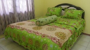 A bed with a green floral bedspread and matching pillows, a wooden headboard, and a window with curtains.