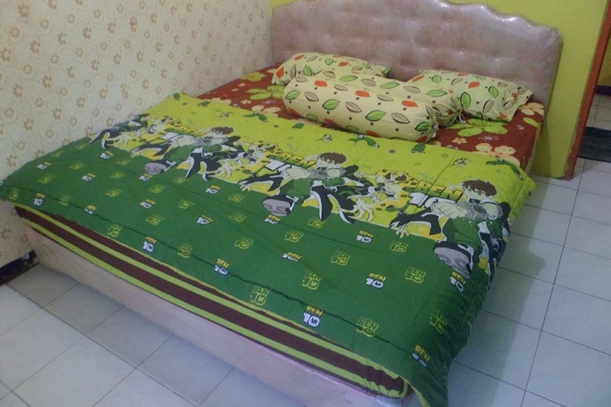 A bed with a floral bedspread and two pillows, a patterned wall, and a tiled floor.
