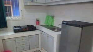 A compact kitchen with white cabinets, a gas stove, a sink, and a refrigerator. - Villa Kota Bunga Matahari (Cipanas)