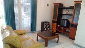 A living room with a sofa, a coffee table, a television, and a cabinet. - Villa Kota Bunga Matahari (Cipanas)