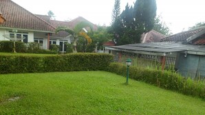 A well-maintained grassy area with a lamp post, surrounded by a hedge and a building with a tiled roof. - Villa Kota Bunga Matahari (Cipanas)