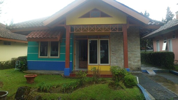 A two-story house with a tiled roof, a front porch, and a small garden area. - Villa Kota Bunga Matahari (Cipanas)