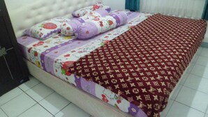 A bed with a patterned bedspread, pillows with Hello Kitty designs, and a red blanket with a monogram pattern. - Villa Kota Bunga Matahari (Cipanas)