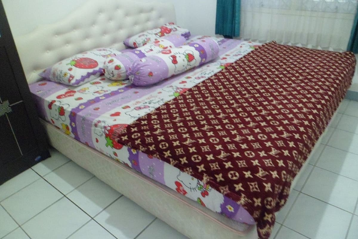 A bed with a patterned bedspread, pillows with Hello Kitty designs, and a red blanket with a monogram pattern.