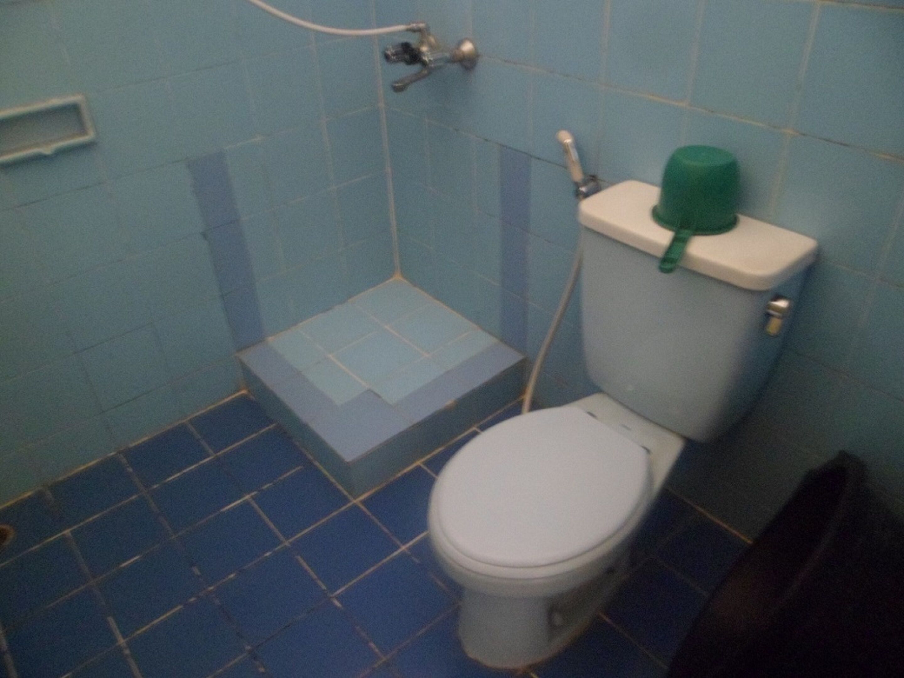 A small bathroom with a toilet, a step stool, and a green bottle on the tank.