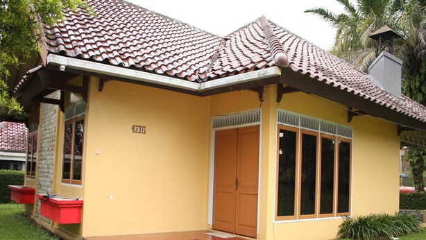 Una casa de dos pisos con techo de tejas, puerta principal y un pequeño jardín delantero.