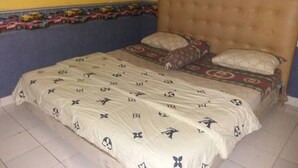 Una cama con colcha estampada y dos almohadas, cabecera capitonada y pared amarilla con un borde decorativo.