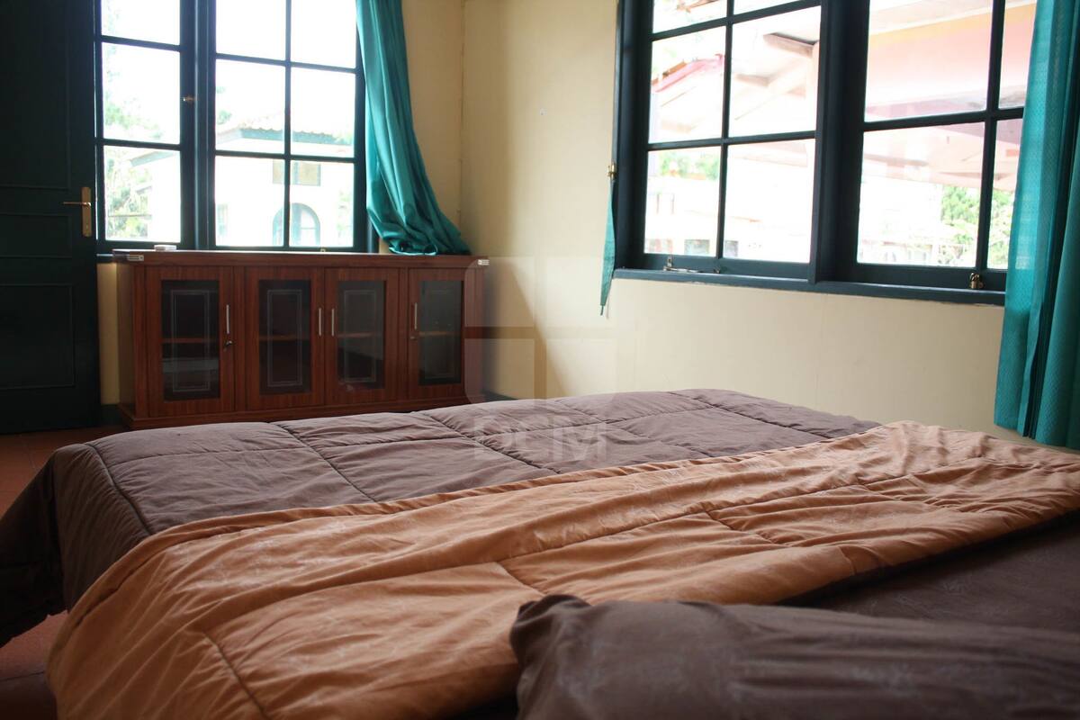 A bedroom with a bed, a wooden cabinet, and two windows with curtains.