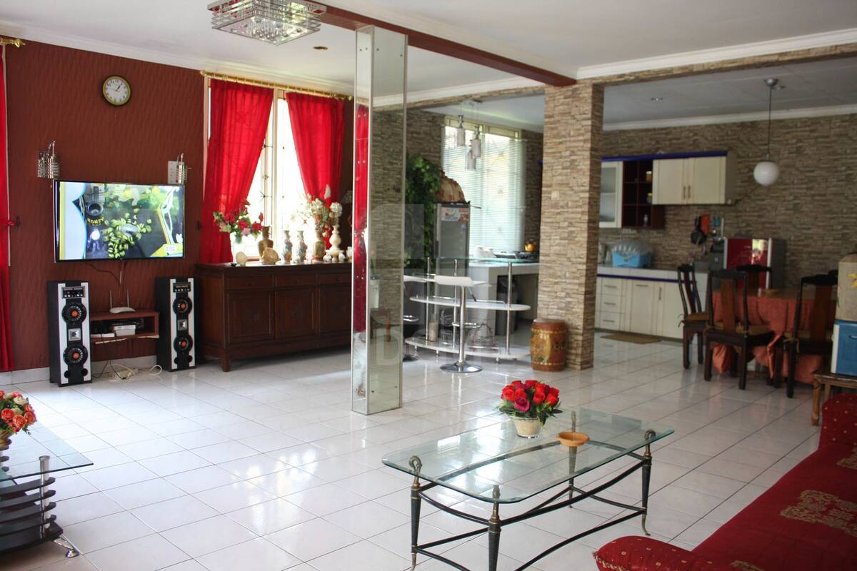 A spacious living area with a glass coffee table, red curtains, a TV, and a kitchen in the background.