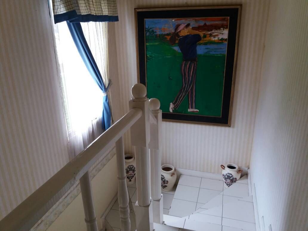 A staircase with a framed painting of a golfer, a window with curtains, and a small table with cups and saucers.