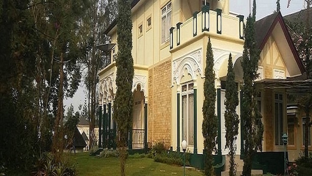 Een gebouw met twee verdiepingen, een symmetrische gevel, een centrale ingang met een decoratieve boog en een kleine tuin met geknipte gras en enkele bomen.