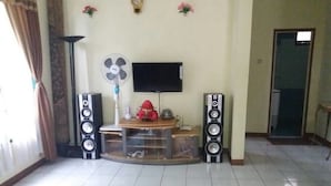 Een woonkamer met een televisie, twee speakers, een ventilator en een klein tafeltje met decoratieve objecten.
