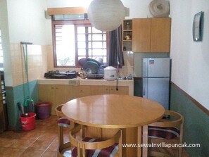 Une cuisine de taille réduite, avec une table et des chaises en bois, un réfrigérateur et une fenêtre avec des rideaux.