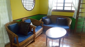Una habitación con dos sofás de mimbre con cojines azules, una mesa redonda de madera y una ventana con diseño de cuadrícula.