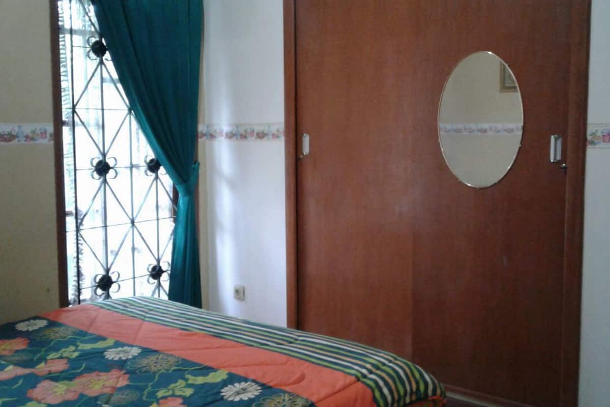Un dormitorio con cama, armario de madera, espejo y ventana con cortinas.