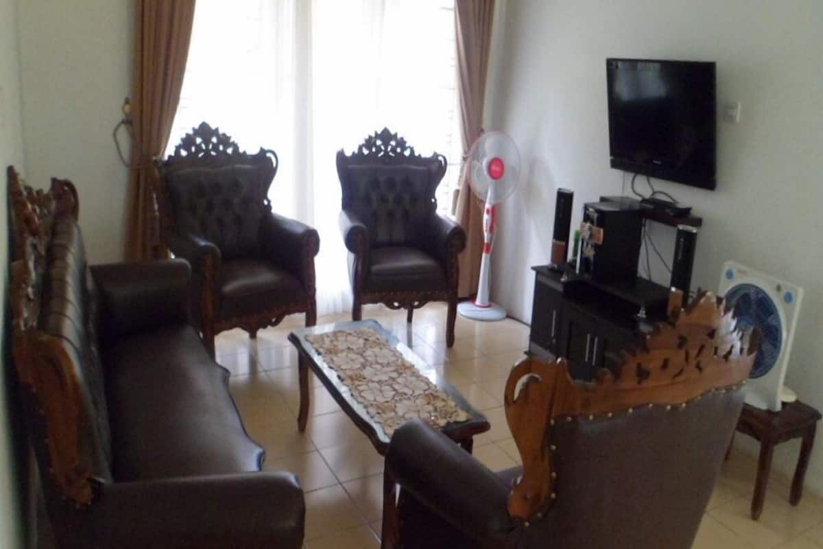 Una sala de estar con un sofá, dos sillones, una mesa de centro, un televisor y un ventilador.