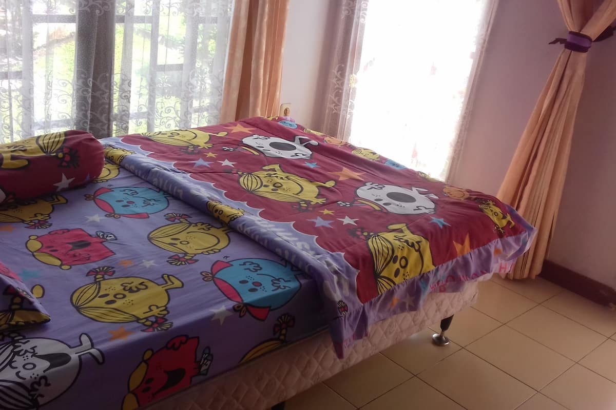 Una cama con ropa de cama colorida que presenta personajes de dibujos animados, una ventana con cortinas y un suelo de baldosas.