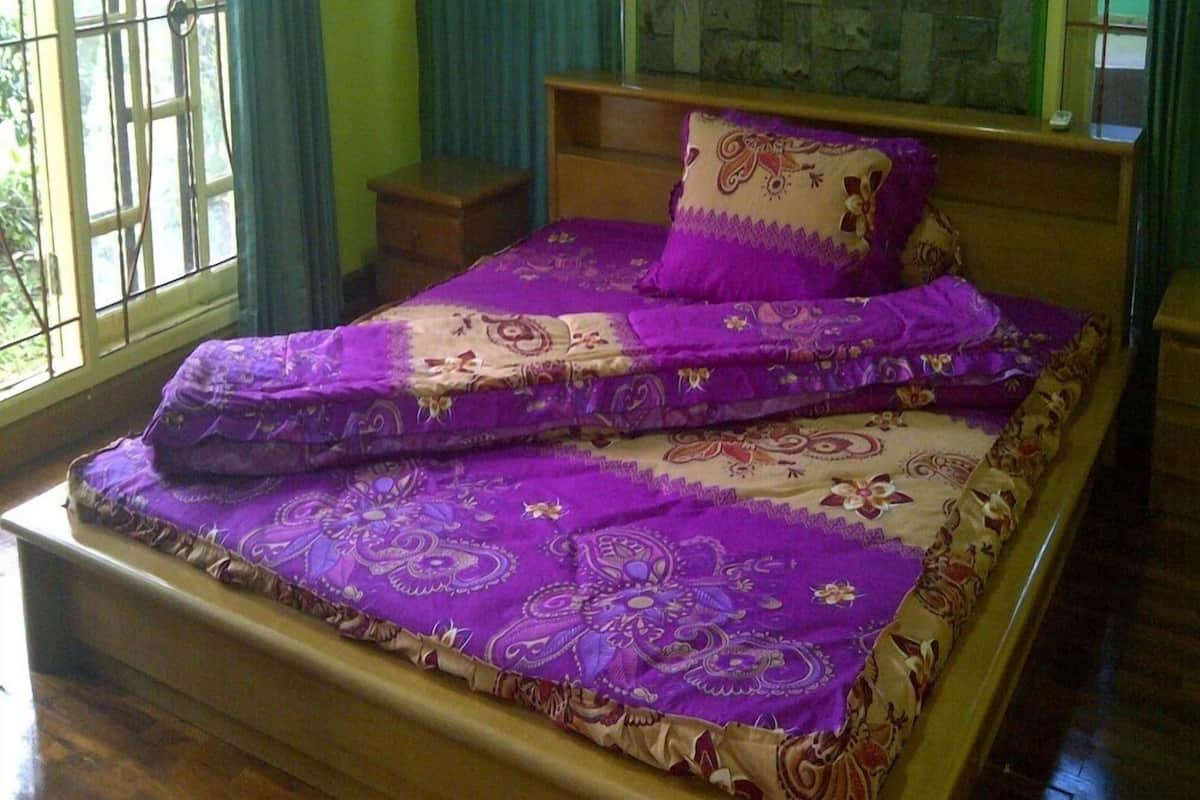 Un dormitorio con una cama cubierta por una colcha estampada en tonos morado y beige, un cabecero de madera y una mesita de noche pequeña.