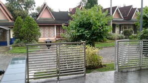 A traditional-style building with a tiled roof and a garden area with a metal fence. - Villa Kota Bunga Teratai (Cipanas)