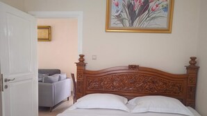 Ein Schlafzimmer mit einem hölzernen Kopfteil, einem Bett mit weißen Bettwäsche, einem grauen Sofa und einem gerahmten Gemälde an der Wand.