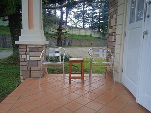 A covered patio area with two metal chairs and a small wooden table, surrounded by stone and brick walls. - Villa Kota Bunga Anyelir (Cipanas)