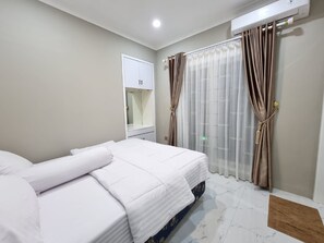 A bedroom with a bed, a wardrobe, a mirror, and curtains. - Villa Kota Bunga Anyelir (Cipanas)