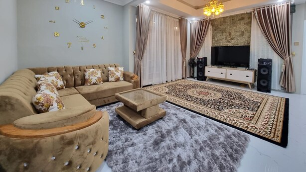 A modern living room with a sectional sofa, a coffee table, a large rug, a TV, and speakers. - Villa Kota Bunga Anyelir (Cipanas)