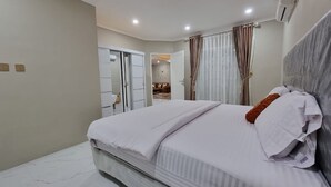 A modern bedroom with a large bed, a wardrobe, and a bathroom visible through an open door. - Villa Kota Bunga Anyelir (Cipanas)