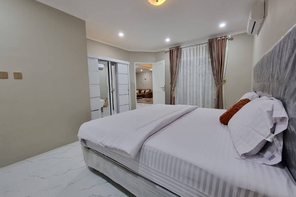Un dormitorio moderno con una cama grande, un armario y un baño visible a través de una puerta abierta.