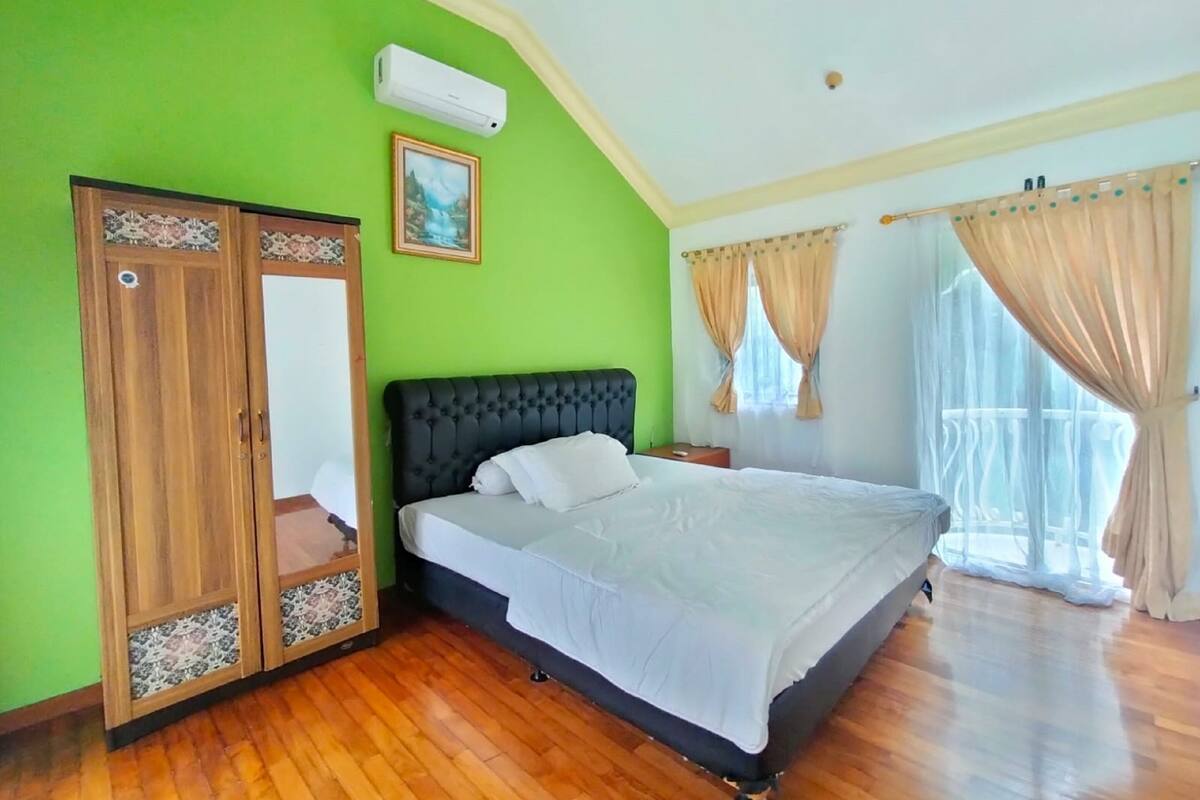 A bedroom with a bed, a wardrobe, a painting, and a window with curtains.