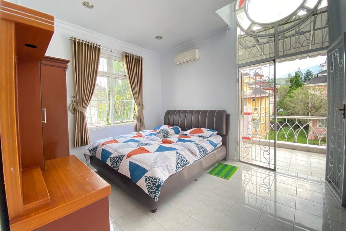 A bedroom with a bed, a wardrobe, a window with curtains, and a balcony with a view.