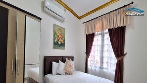 A bedroom with a bed, a wardrobe, an air conditioner, a painting, and curtains. - Villa Kota Bunga Allamanda (Cipanas)