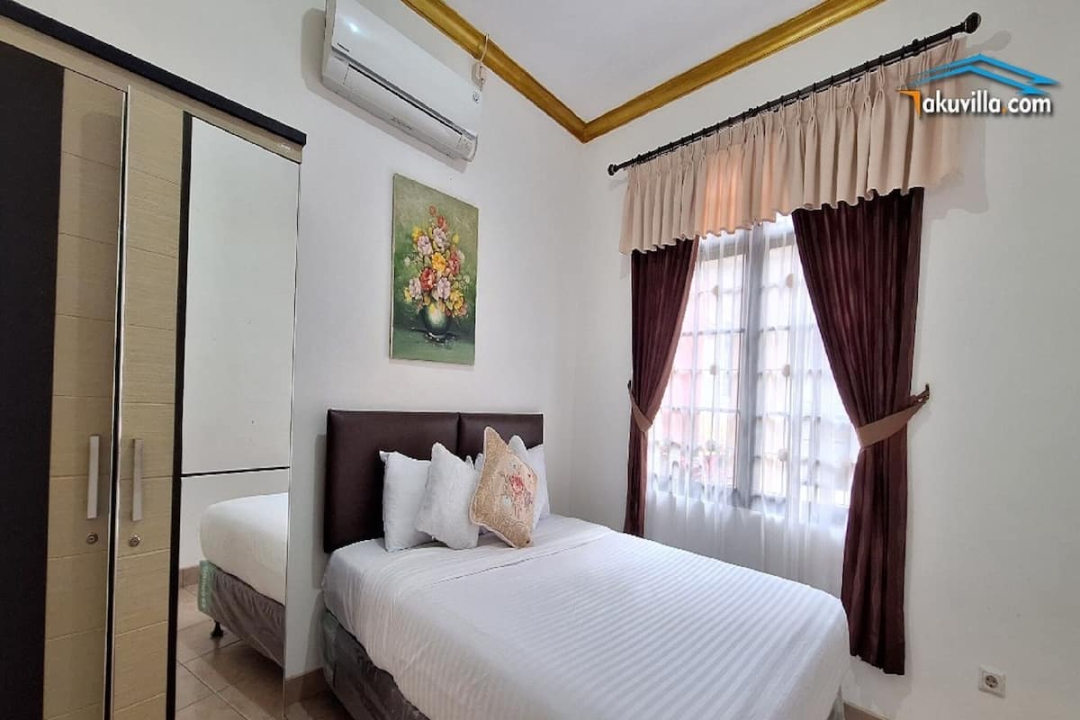 A bedroom with a bed, a wardrobe, an air conditioner, a painting, and curtains.