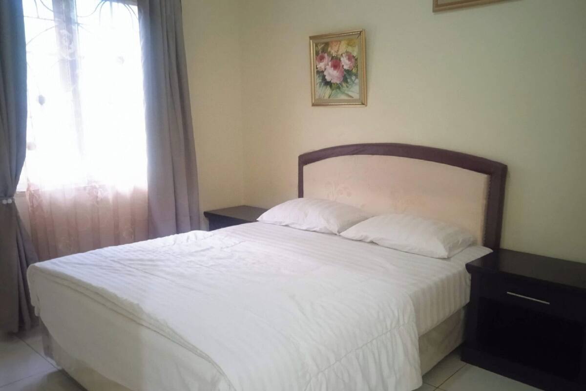 A neatly made bed with white linens in a room with a tiled floor.