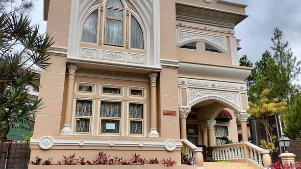 A large, ornate building with a grand entrance, multiple windows, and a staircase leading to the main entrance. - Villa Kota Bunga Allamanda (Cipanas)