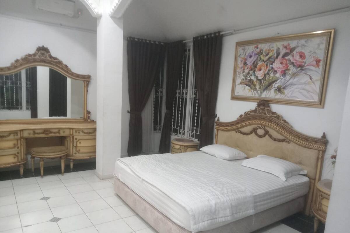 A bedroom with a bed, a dresser, a vanity, and a painting.