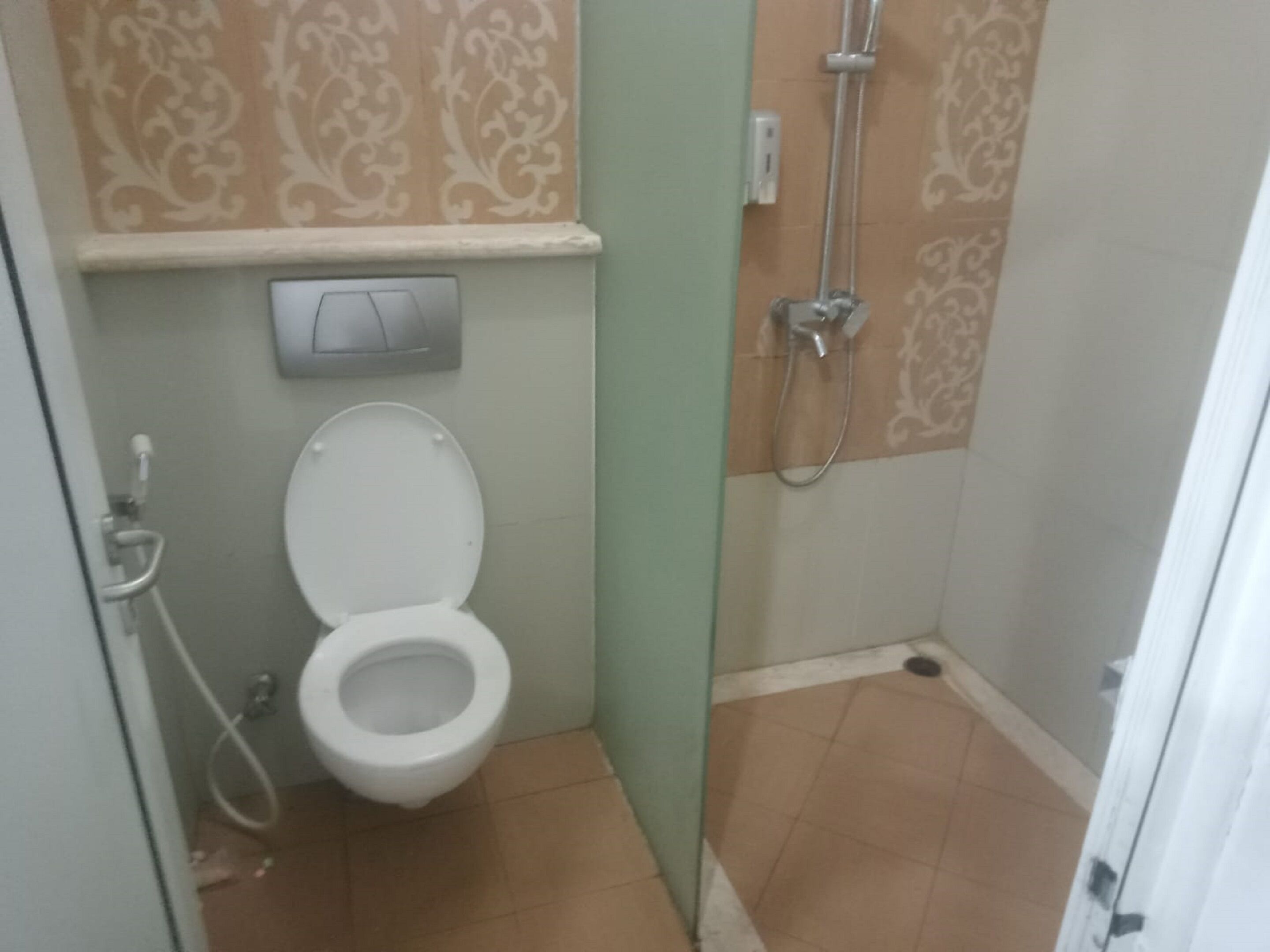 A small bathroom with a toilet, a shower, and a wall-mounted light fixture.