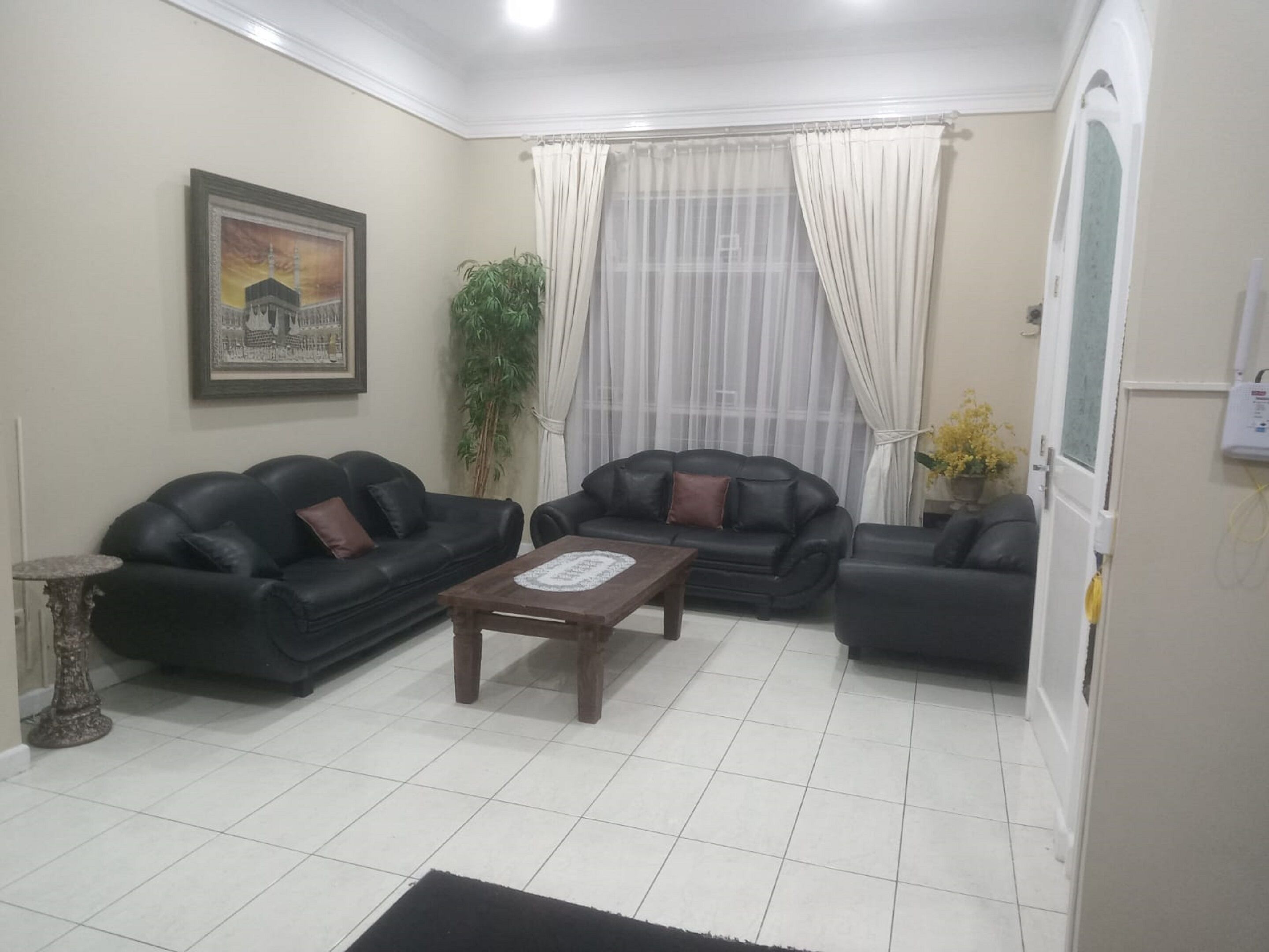 A living room with two black leather sofas, a wooden coffee table, a potted plant, and a framed picture on the wall.