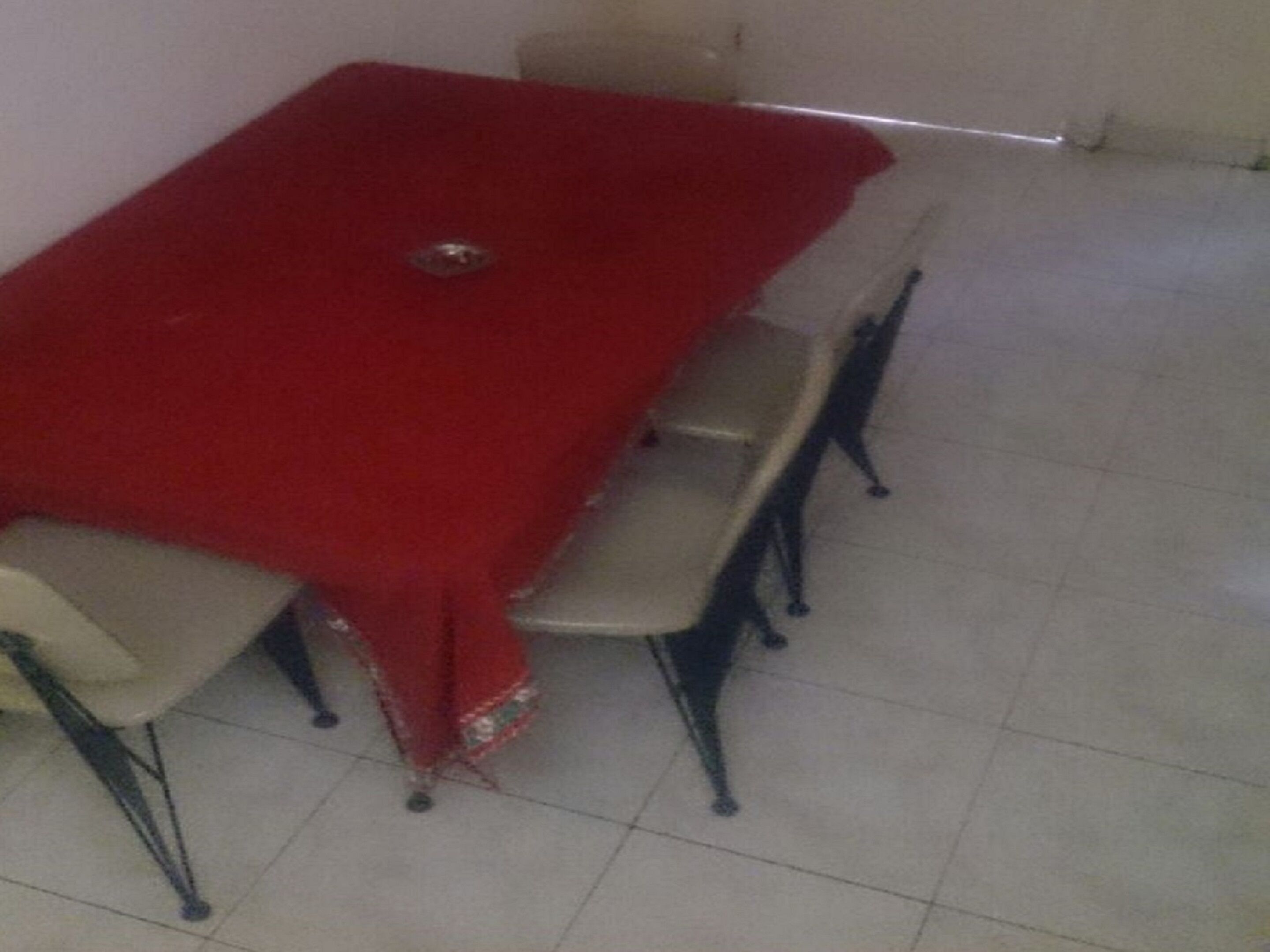 A dining table with a red tablecloth, four chairs, and a small decorative item on the table.