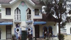 A two-story house with a balcony on the second floor, a front door, and a small garden area. - Villa Kota Bunga Vinca (Cipanas)