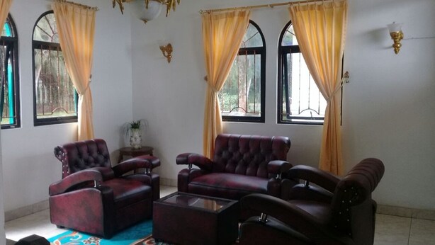 A spacious living room with a large sofa set, a coffee table, and a chandelier. There are two windows with curtains, and a small table with a plant. - Villa Kota Bunga Vinca (Cipanas)