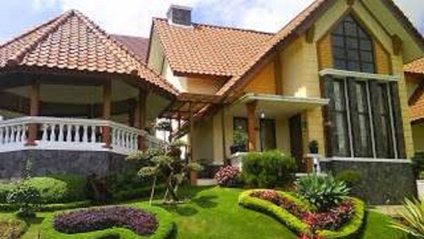 Una casa de dos pisos con techo de tejas, un balcón y un jardín bien cuidado con diversas plantas y arbustos.