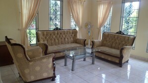 Un salón amplio con dos sofás y una mesa de centro de vidrio, ventanas grandes con rejas de hierro decorativas y piso de baldosas.