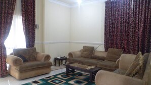 A living room with two beige sofas, a patterned rug, and curtains. - Villa Kota Bunga Mawar (Cipanas)